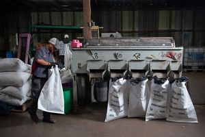 A person attaches large white sacks to a seed-sorting machine.