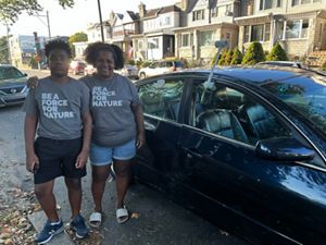 A woman and her son pose in gray shirts that read "be a force for nature" in front of a car.