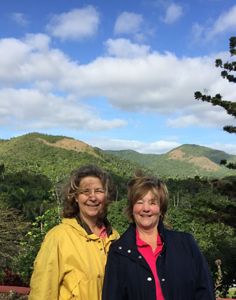 two women posing for a picture with a large green forest behind them.