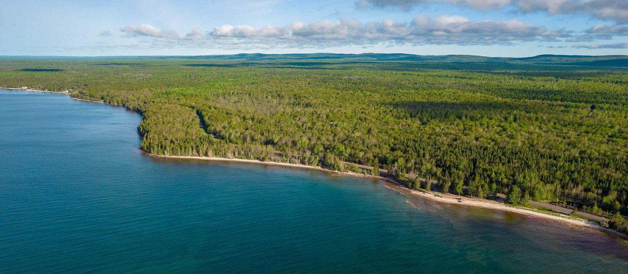 Aerial view of the still water of Lake Superior along the wooded Little Betsy Shoreline in the Keweenaw on a clear day. 