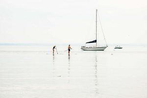Two people paddling on calm water near a bigger boat. 