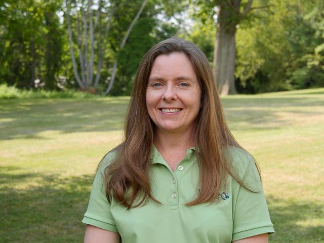Michelle Canick headshot. A smiling woman in a pale green shirt stands in an open park space with trees behind her.