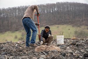 Two volunteers plant a tree on a rocky hilltop.