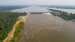 River surrounded by woods with a lock and dam and a bridge in the background.