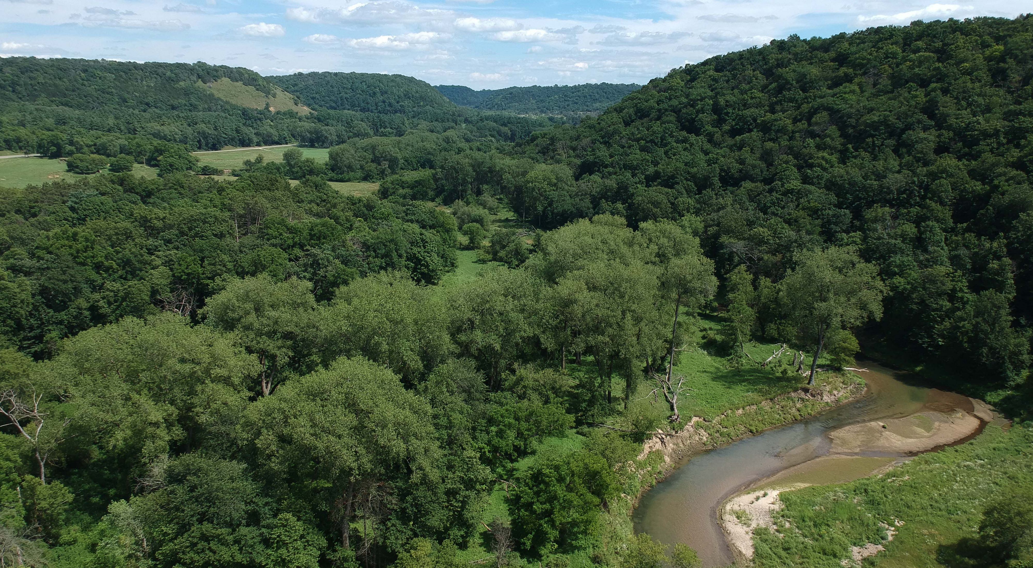 River winding through a forest with patches of open grassland in Minnesota’s driftless area.