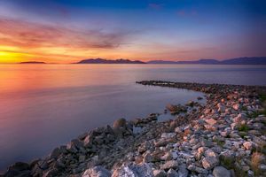 Looking across the Great Salt Lake at sunset; a rock jetty extends out into the lake, and the water is various shades of orange and blue.
