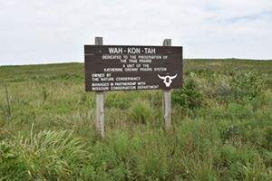 A wooden sign with preserve name 'Wah-Kon-Tah' on it sits in an open prairie field.