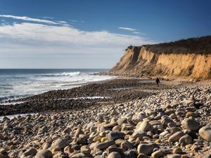 A view of Montauk bluffs and the shoreline with waves of water crashing into a rocky beach. 