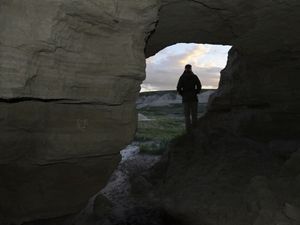 a person looks out over the prairie from an opening in the crag.