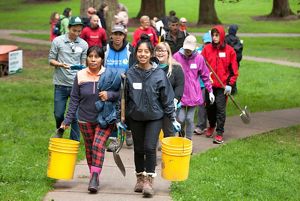 A diverse group of volunteers walks along a trail in Mount Tabor Park in Portland carrying buckets, shovels and gloves.