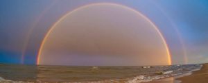 A double rainbow arcing over waves washing up on the beach.