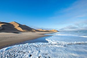A desert landscape meets up with waves crashing along the coast.