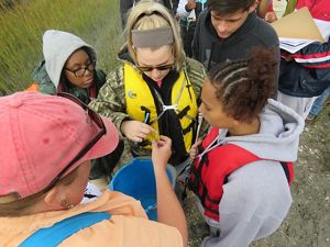 View looking down on four students crowding around a TNC staff member who is holding out a small fiddler crab for them to see. 