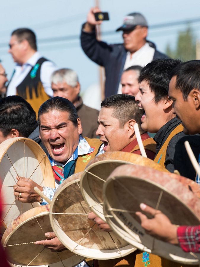 A group of eight men are yelling and beating drums