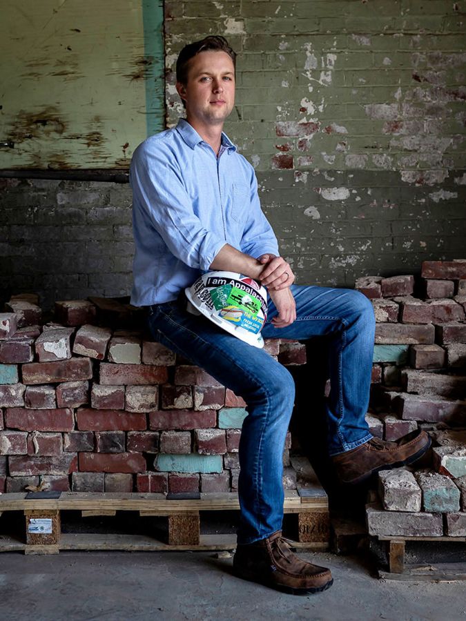 man holds a hardhat, sits on a pile of reclaimed bricks