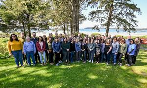 a group of about 30 diverse people posed in front of a scenic mountain view and smiling