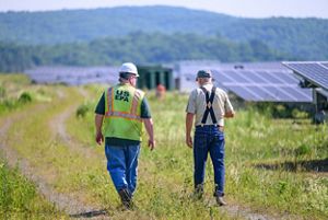Two men walk along the edge of a field of solar panel arrays.