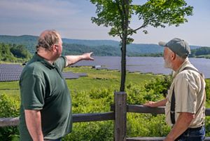 Two people stand and talk in front of solar panels. 