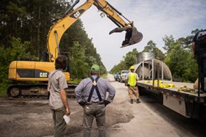 Excavator lifting water control structure from delivery truck at Angola Bay.