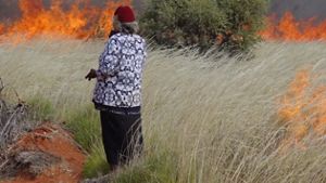 A woman standing in a burning grassland.