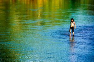 A smiling girl walks slowly with her bare feet in a river at sunset.