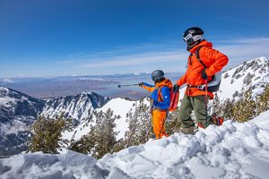Two brightly dressed skiers on top of mountain looking downslope. 