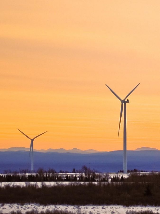 Two wind turbines set against hillside and orange sky.