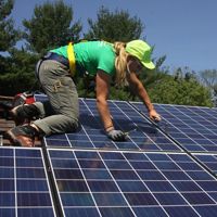 A woman in a green shirt kneels as she installs solar panels.