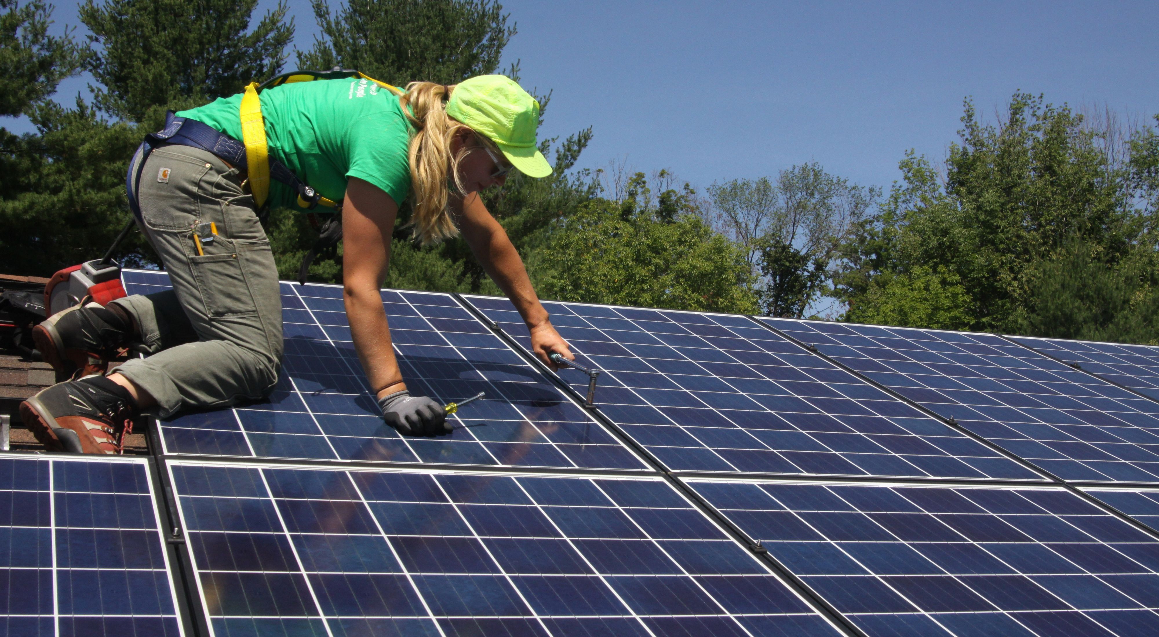 A worker installs solar panels on a roof during a sunny day. 