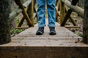A close-up of a hiker's shoes on a wooden bridge in the woods.