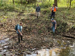 Four people stand in degraded stream bed in forest.