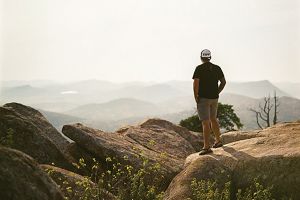 Man standing on mountain rocks overlooking the valley.