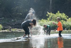 Two adults and two children standing in a river and playfully splashing each other.