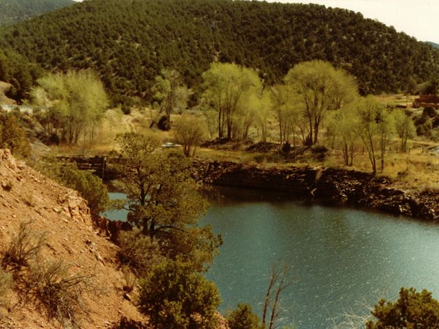 Old photo of stone dam on river in front of forested mountain.