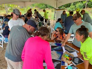 a group of people gather around a table examining various maps on it.