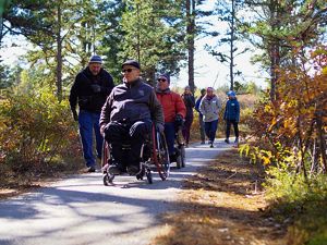 A group including a man using a wheelchair make their way down a path in the woods.