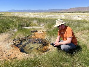 A man kneeling down next to a water hole.