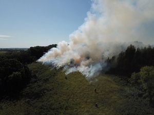 An aerial view of a fire with lots of smoke at the top of a grassland hill.