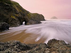 A time-lapse photo of waves coming in at a sandy beach bordered by rugged boulders and cliffs.