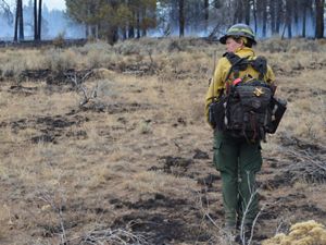 TNC Oregon Fire Manager Katie Sauerbrey stands in fire practitioner gear in front of a forest
