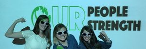 Three TNC employees flex at the camera as they stand in front of a sign that says 'Our People Our Strength.'