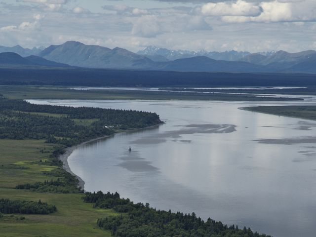 Aerial view of Bristol Bay, showing green forest in the foreground and mountains beyond the water.
