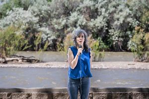 A woman speaking into a microphone in front of a river.