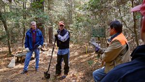 Three men stand in a forest clearing talking during a stewardship workday.