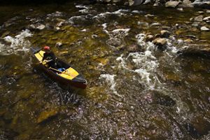 A person paddling a yellow canoe in a river.