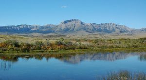 A mountain range rises out of a flat plain with a body of water in the foreground.