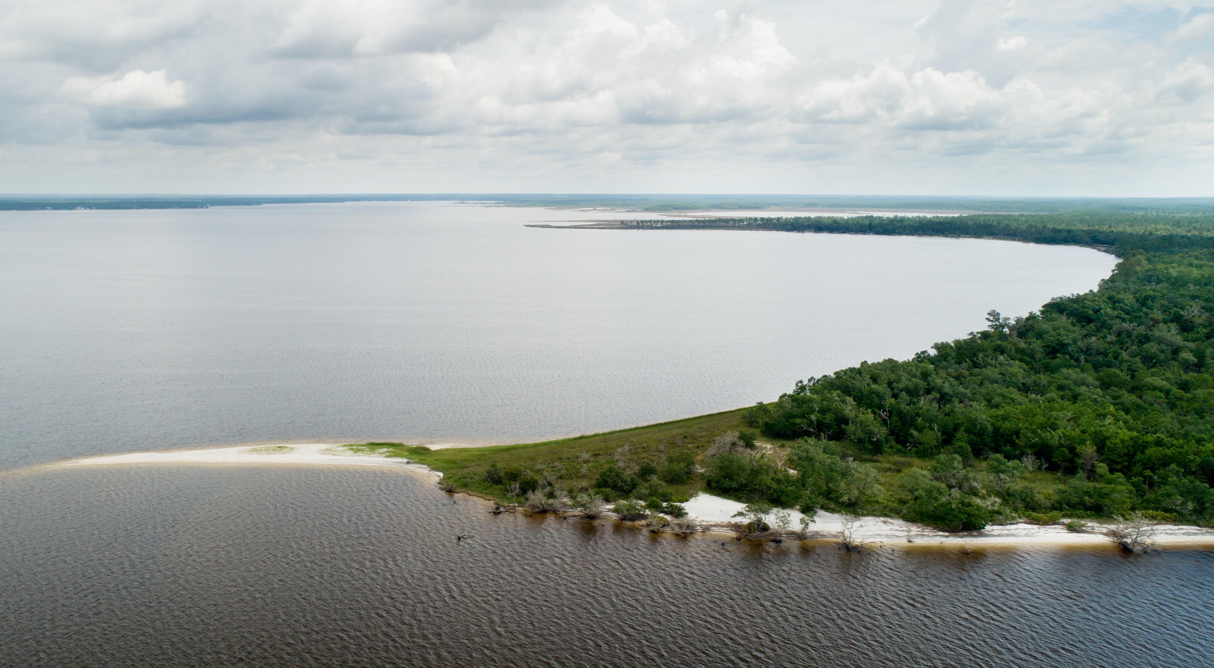 Scenic aerial landscape of the Pensacola Perdido Watershed bay area with bay water and green forested shoreline.