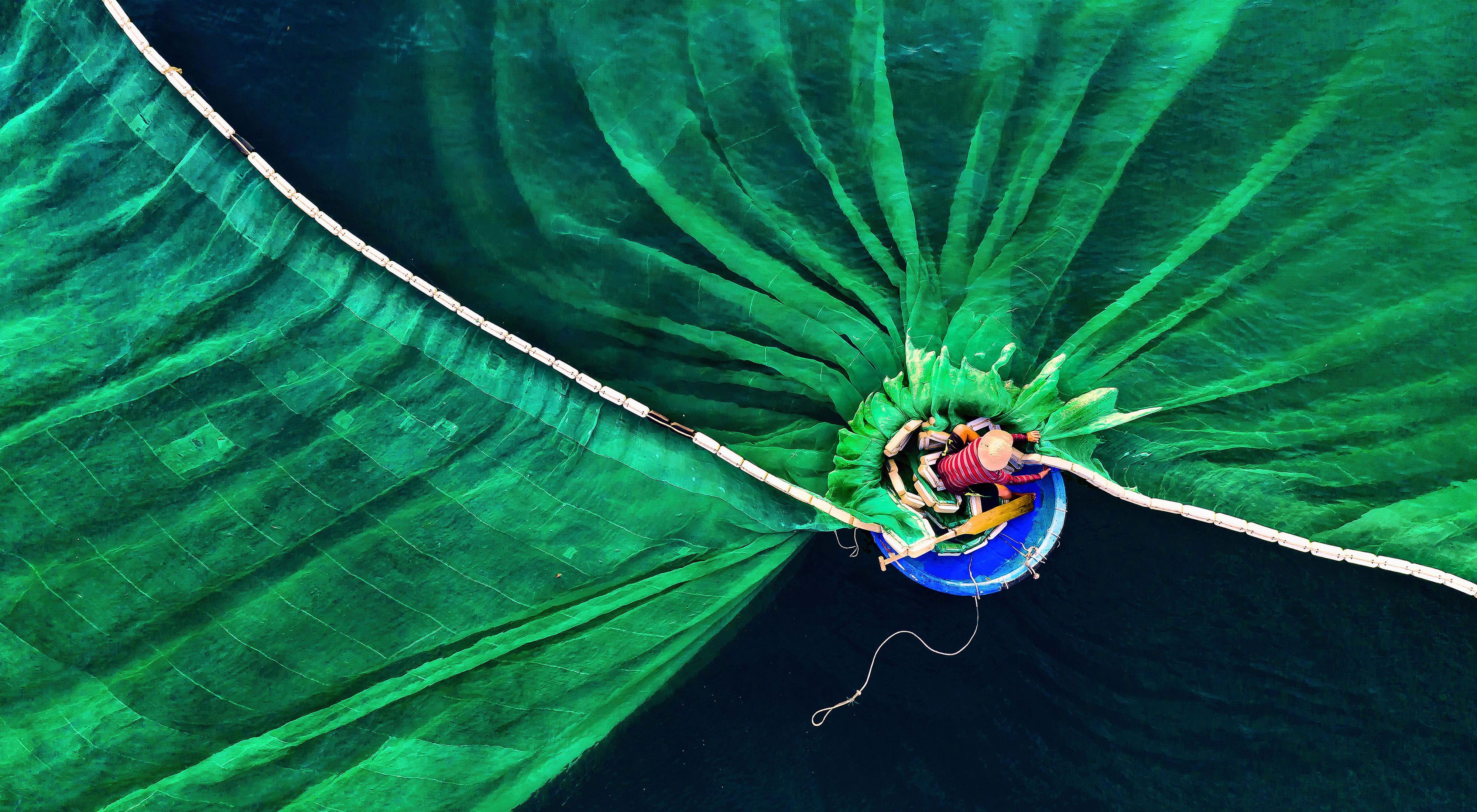 Una persona en una pequeña embarcación circular lanza una enorme red de pesca al agua.