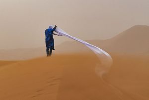A guide in the Sahara Desert during a sand storm. The person's long, unraveled head wrap blows to the side into the sand.