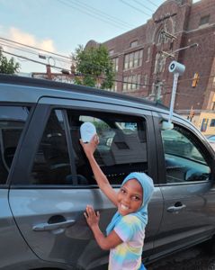 A young girl holds a heat measuring device onto a car window. 